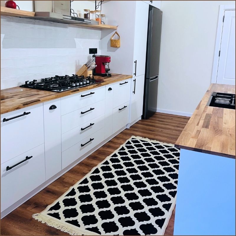 black and white kitchen with black accents, open wood shelves, and woven rug.