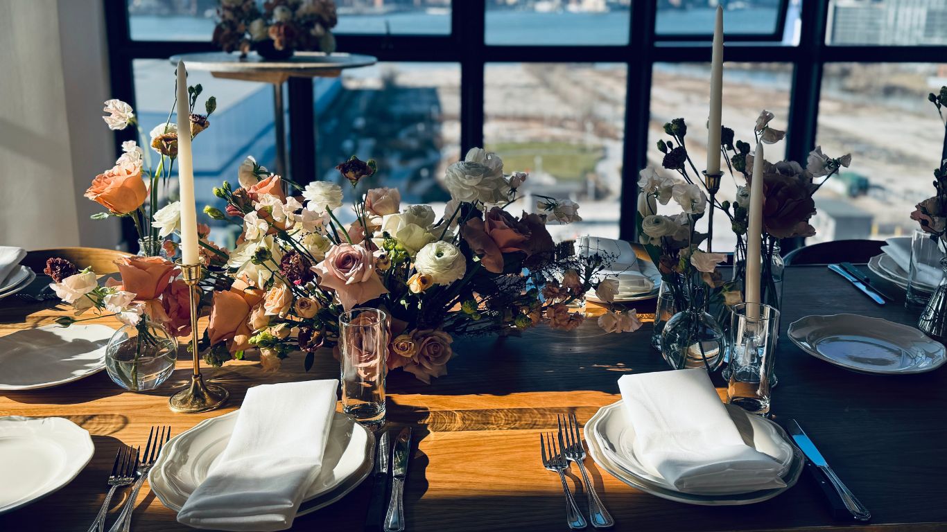 Modern elegant table setting with white plates, floral centerpiece and city skyline view through windows