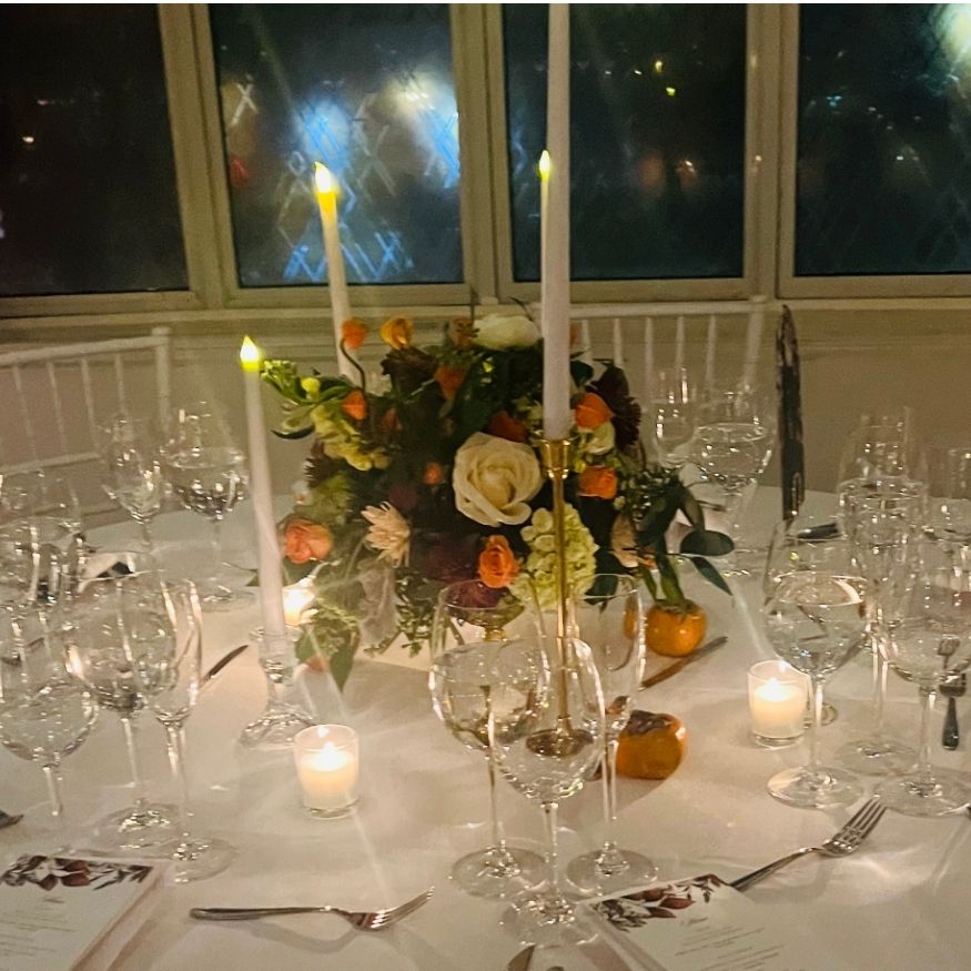 Evening dinner table with brass taper candle holders, glass votives, and floral centerpiece in warm candlelight