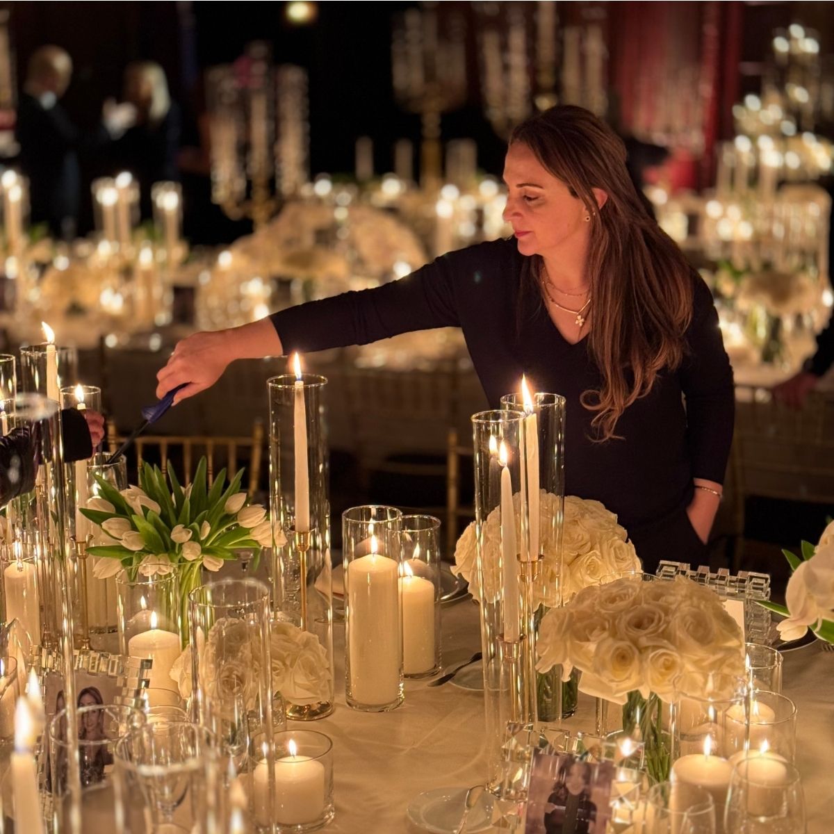Professional table setter lighting candles at elegant dinner event with white roses and crystal glassware
