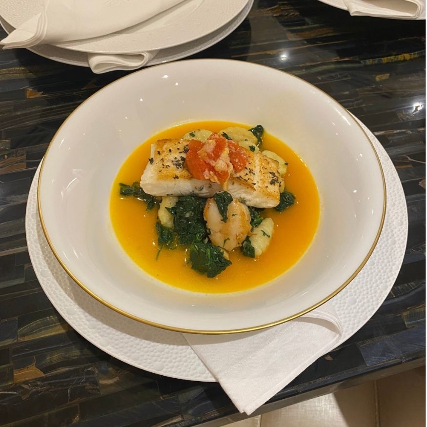 White fish served in elegant porcelain bowl with gold rim on dark marble table setting