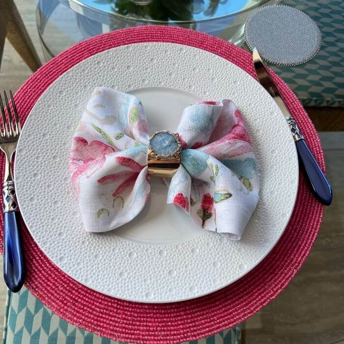 Colorful bow napkin fold with floral linen napkin and decorative ring on pink placemat
