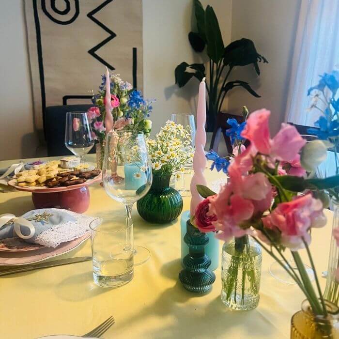 Bud vases for dinner table with spring flowers, candles, and colorful place settings
