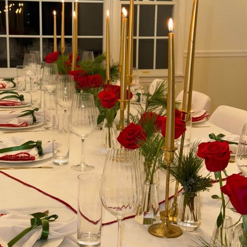 Champagne flutes and wine glasses on holiday dinner table with gold candles and red roses showing glassware for special occasions
