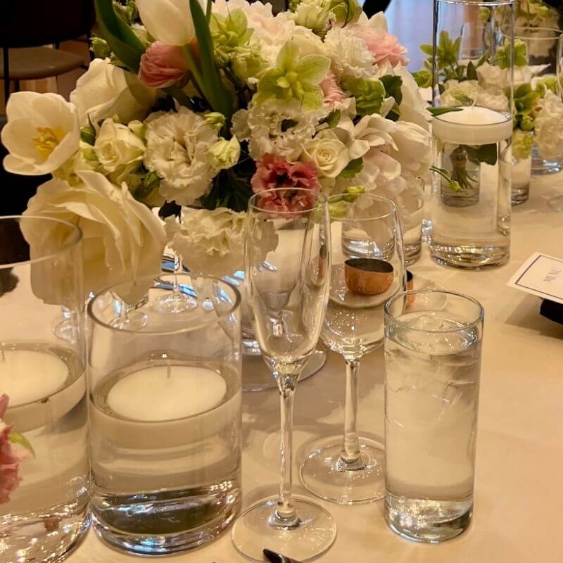Proper glassware place setting showing water glass and champagne flute position on dinner table with spring floral centerpiece