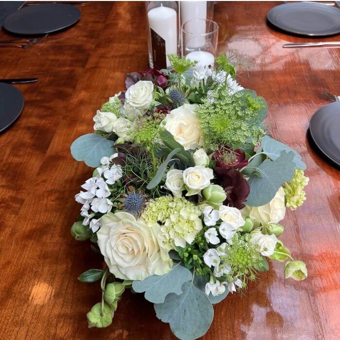 Low centerpiece for dining table with white roses, eucalyptus, and pillar candles