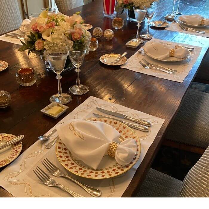 Elegant dinner party table with folded napkins and gold napkin rings on embroidered placemats