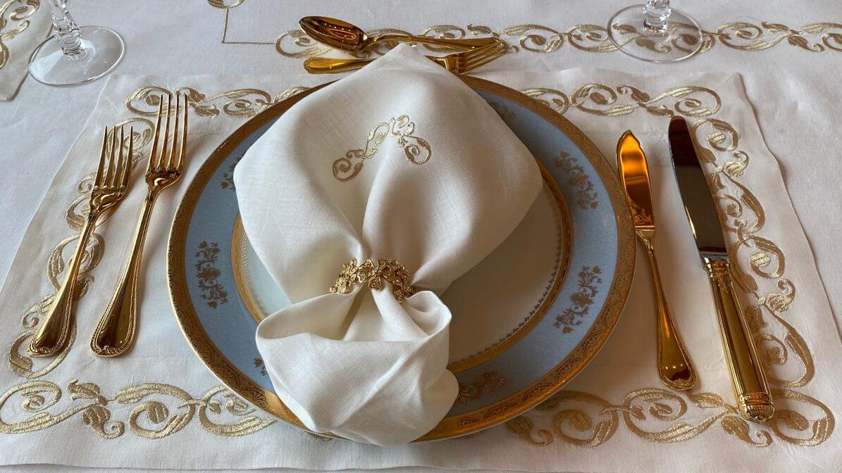 Elegant napkin folding ideas with white linen napkin and gold ring on blue and gold china