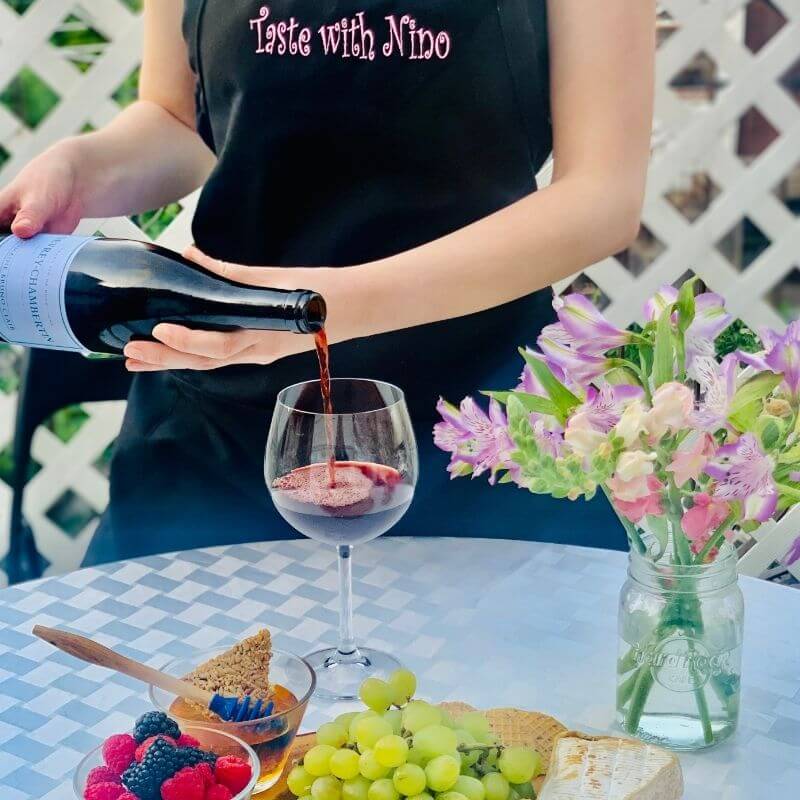 Red wine being poured into stemmed wine glass with cheese board showing proper dinner glassware for entertaining