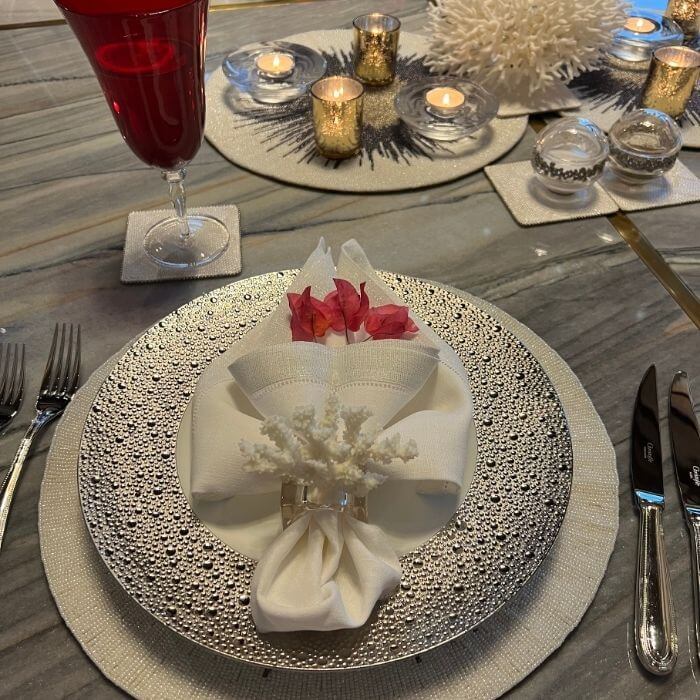 Gathered napkin fold with coral napkin ring and fresh flower accent on silver charger