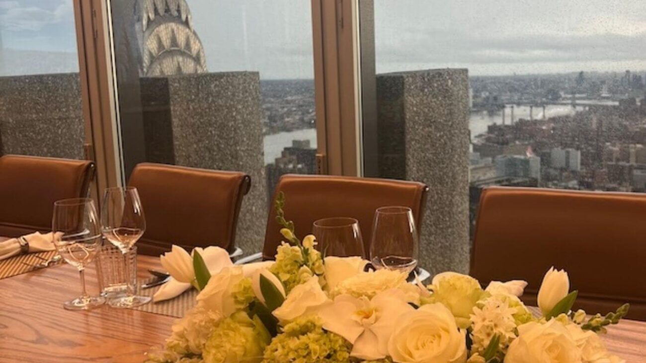 Types of glassware on elegant dinner table including stemmed wine glasses and water glasses with floral centerpiece and NYC skyline view