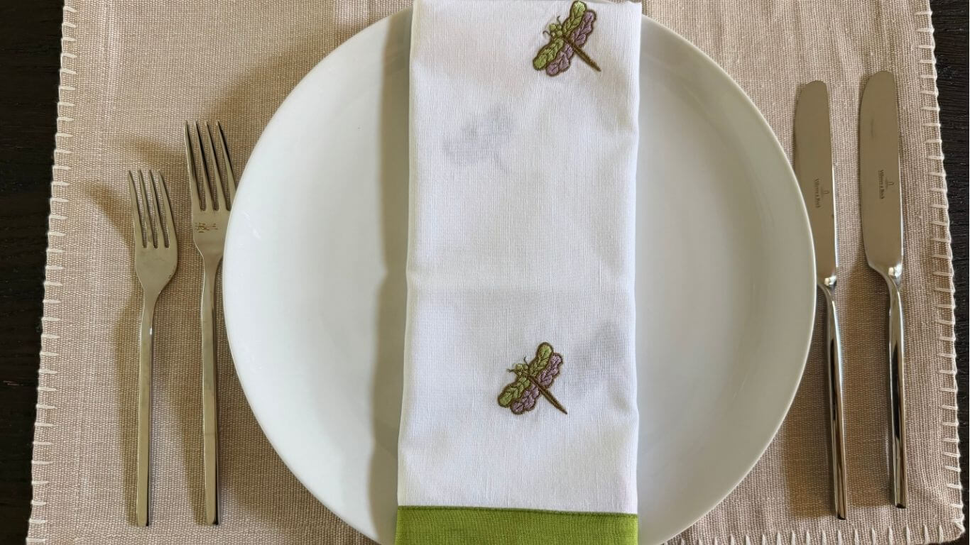 Final place setting for dinner party checklist with white plate, embroidered napkin, and Villeroy & Boch flatware
