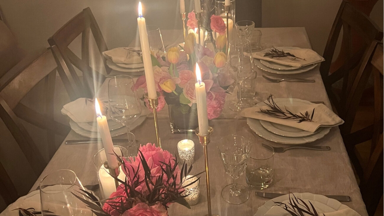 How to host a dinner party — candlelit table styled at home with flowers and layered place settings