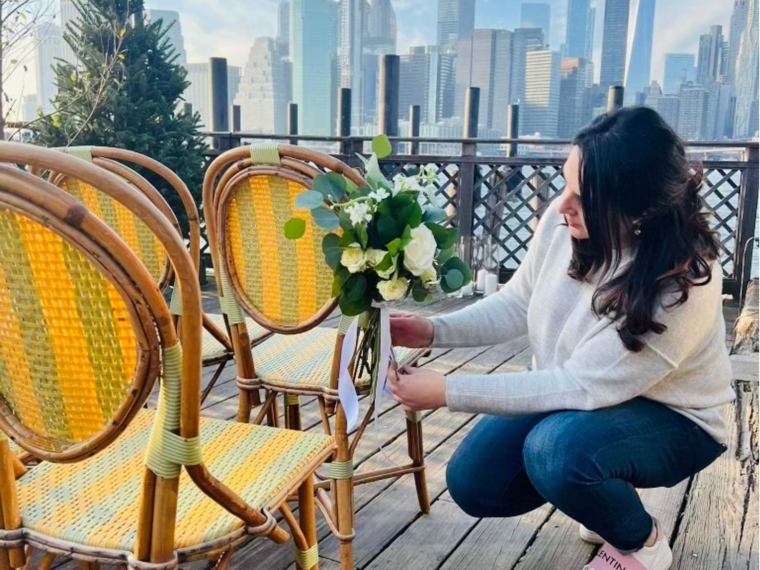 Table stylist Nino Meekma arranging a wedding ceremony at River Café in Brooklyn, with Manhattan skyline in background