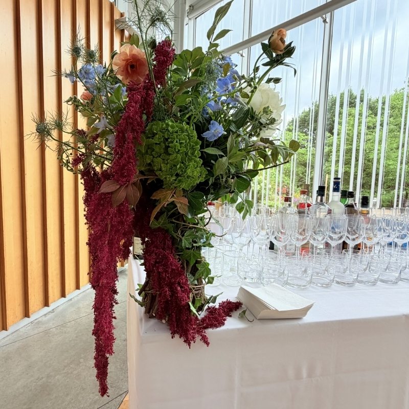 Bar station with a burgundy and blue floral arrangement placed in the far corner beside rows of glassware