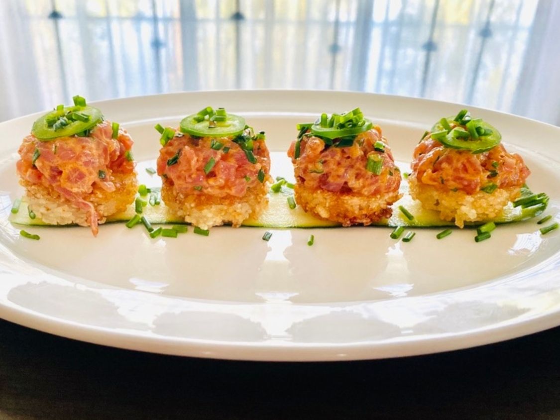 Spicy tuna crispy rice hors d'oeuvres topped with jalapeño slices and chives on a white oval platter