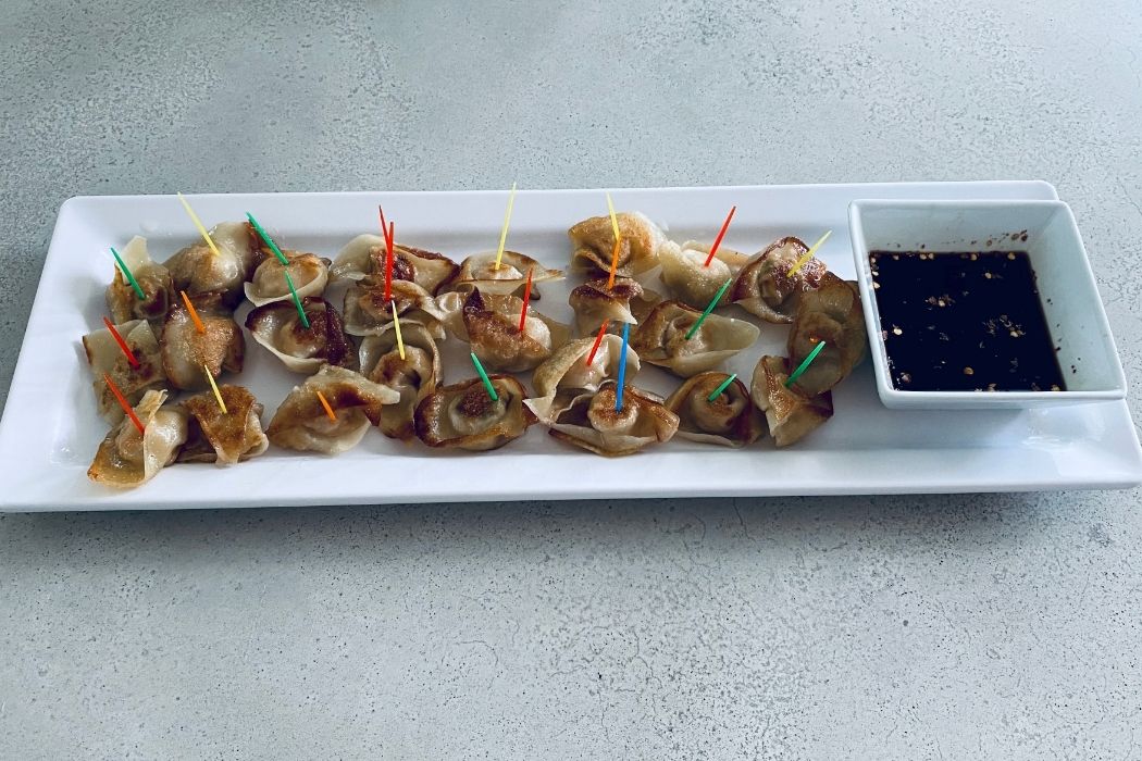 Pan-fried dumplings with colorful cocktail picks on a rectangular white platter with a built-in dipping sauce compartment
