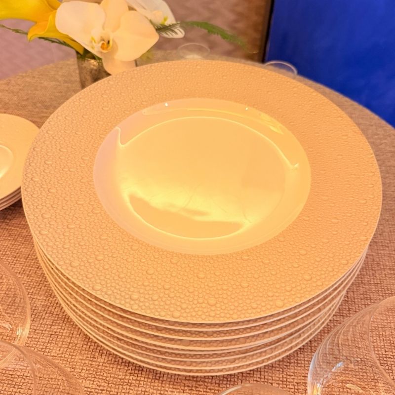 Stack of Bernardaud textured porcelain plates with raised pebble rim beside white orchids