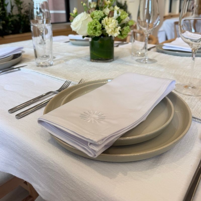 Neutral stoneware plates with a white linen napkin and floral centerpiece on a linen tablecloth