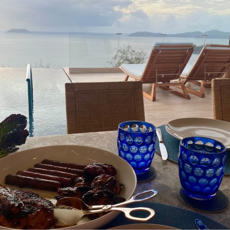 Large serving platter with grilled meat and gold tongs on an outdoor table overlooking the sea
