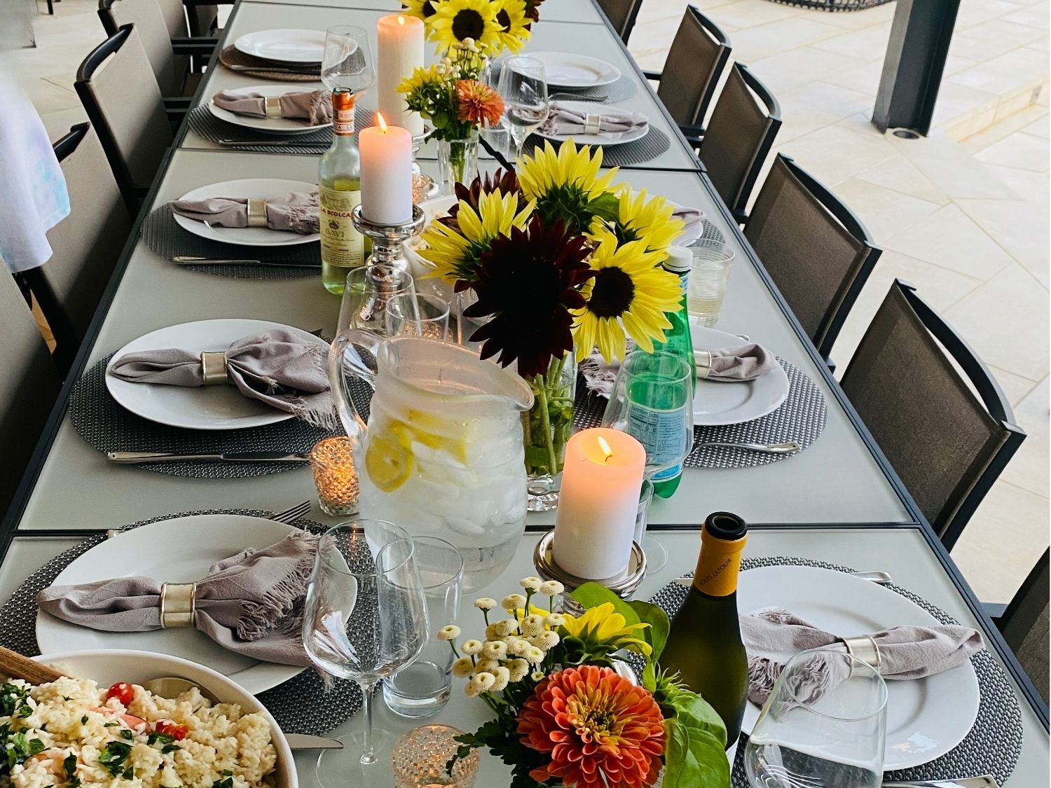 Summer outdoor dinner table with a large white serving bowl, glass pitcher and sunflower centerpieces