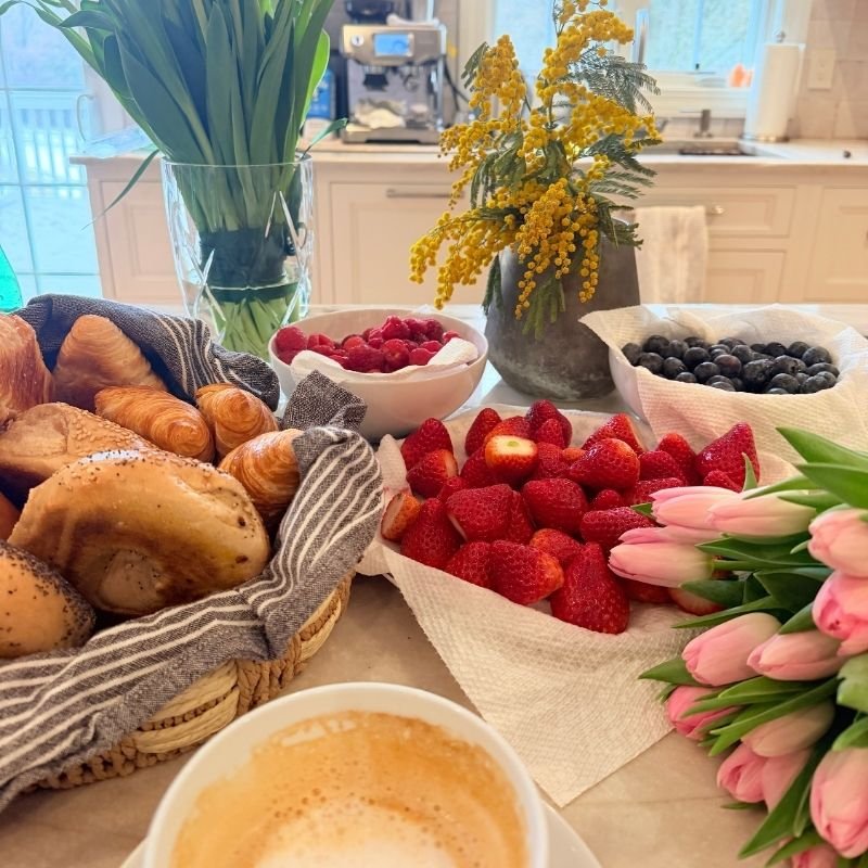 Tulips and mimosa on a kitchen island beside croissants and fresh berries in the morning
