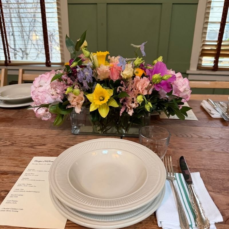 Low white floral centerpiece staying in place while plates and napkins are set around it